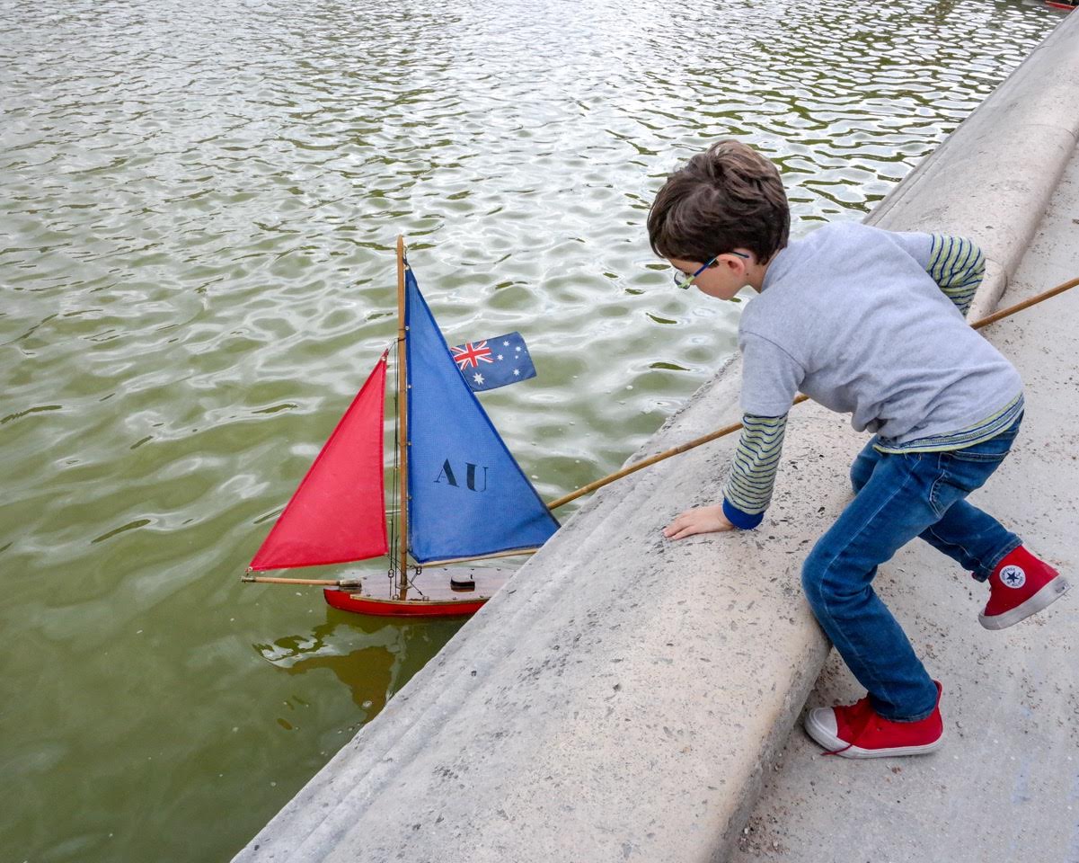 Playing with sailboats in the park water in Paris on a summer family vacation.