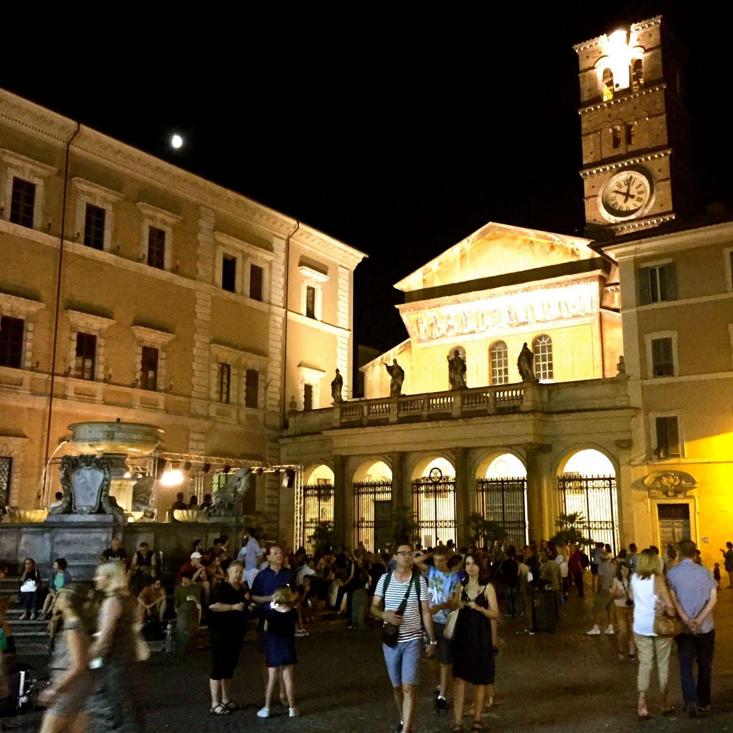 A bustling piazza in Rome lit up at night.