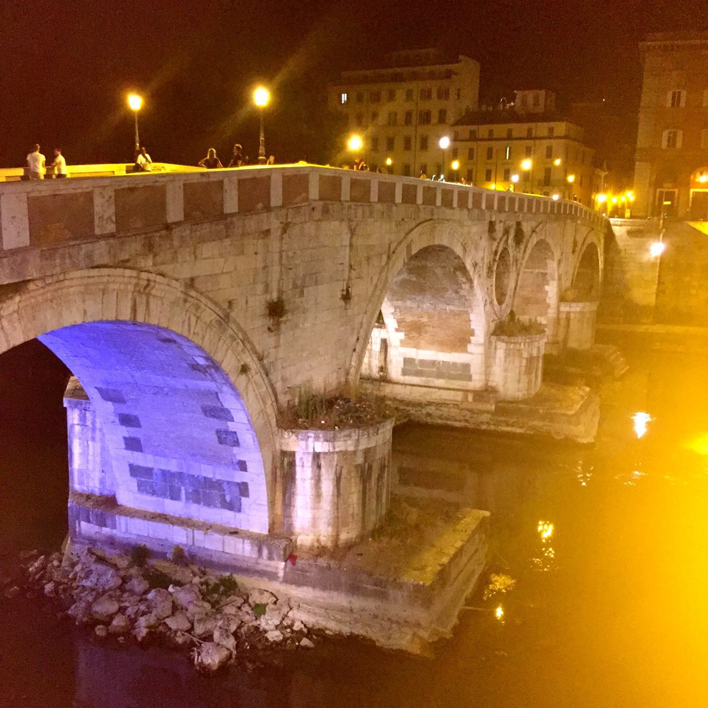 Crossing a bridge lit up at night in Rome to get to Trastevere.